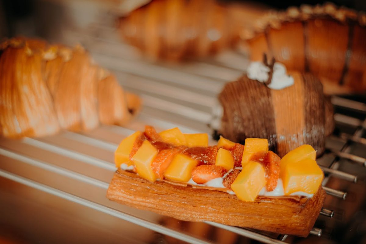 Close-up of a mango-topped pastry surrounded by buttery croissants on cooling rack.